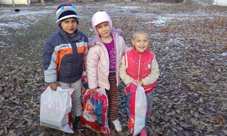 Drei Kinder mit Weihnachtsgeschenktüten auf einem schlammigen Hof