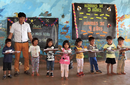 Indigene Erstklässler stehen mit ihren Fibeln im buntbemalten Klassenzimmer